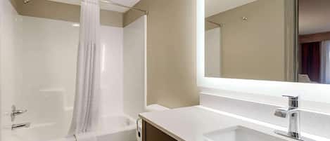 A modern bathroom with a bathtub, toilet, and a large mirror above the sink.