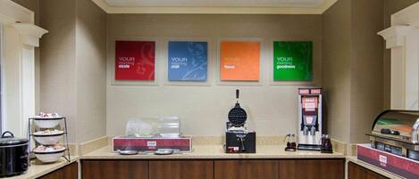 A breakfast bar with a waffle maker, coffee machine, and a self-serve beverage dispenser.