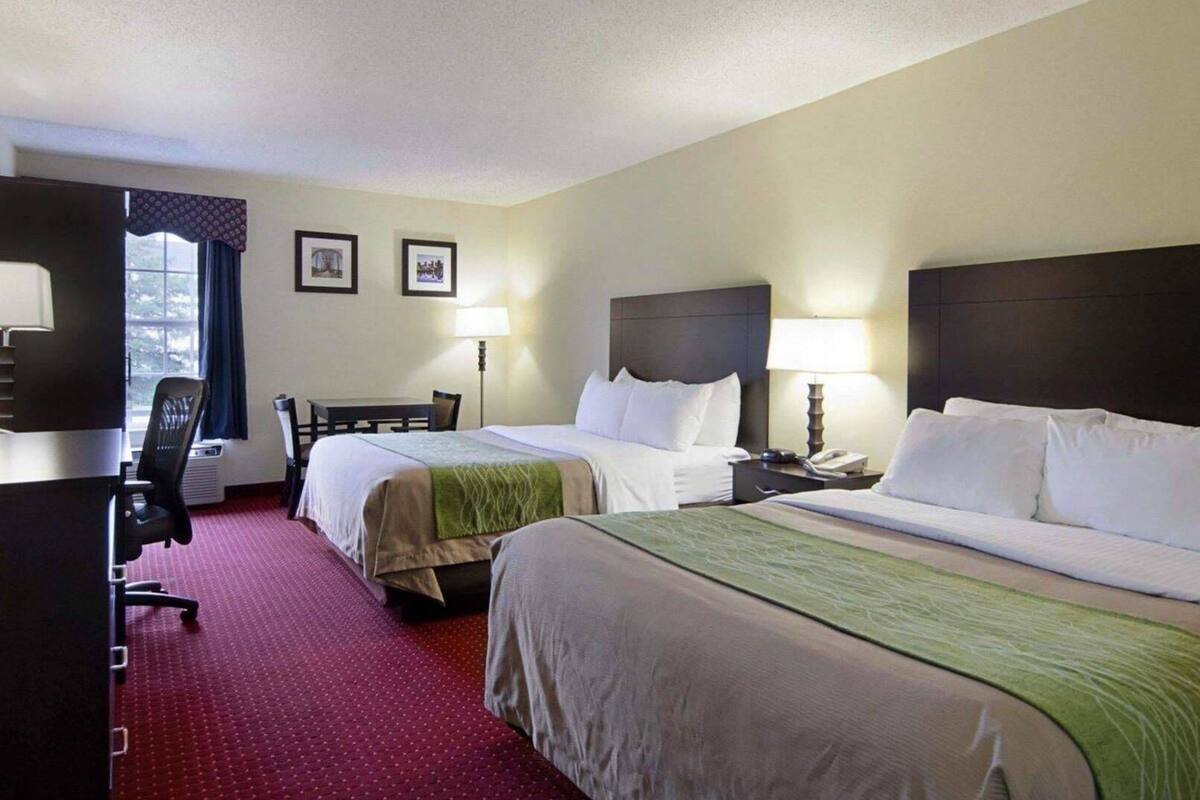 A hotel room with two beds, a desk, a chair, a lamp, and a window with curtains.