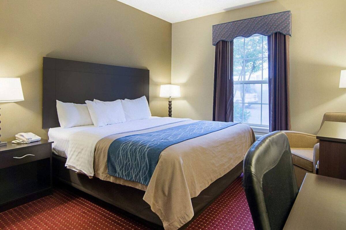 A hotel room with a bed, bedside tables, a desk, and a window with curtains.