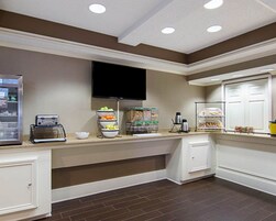 Una cocina de hotel con barra de desayuno tipo autoservicio, una máquina de café y un televisor montado en la pared.