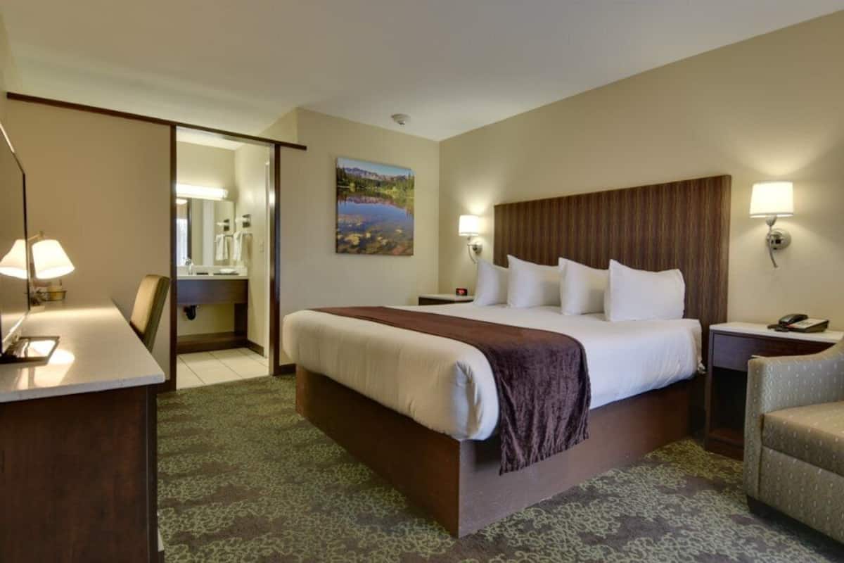 A hotel room with a large bed, bedside lamps, a desk, and a chair.