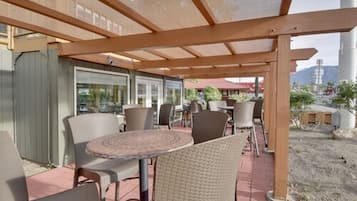 An outdoor patio area with round tables and chairs, wooden pergola, and a view of the surrounding landscape.