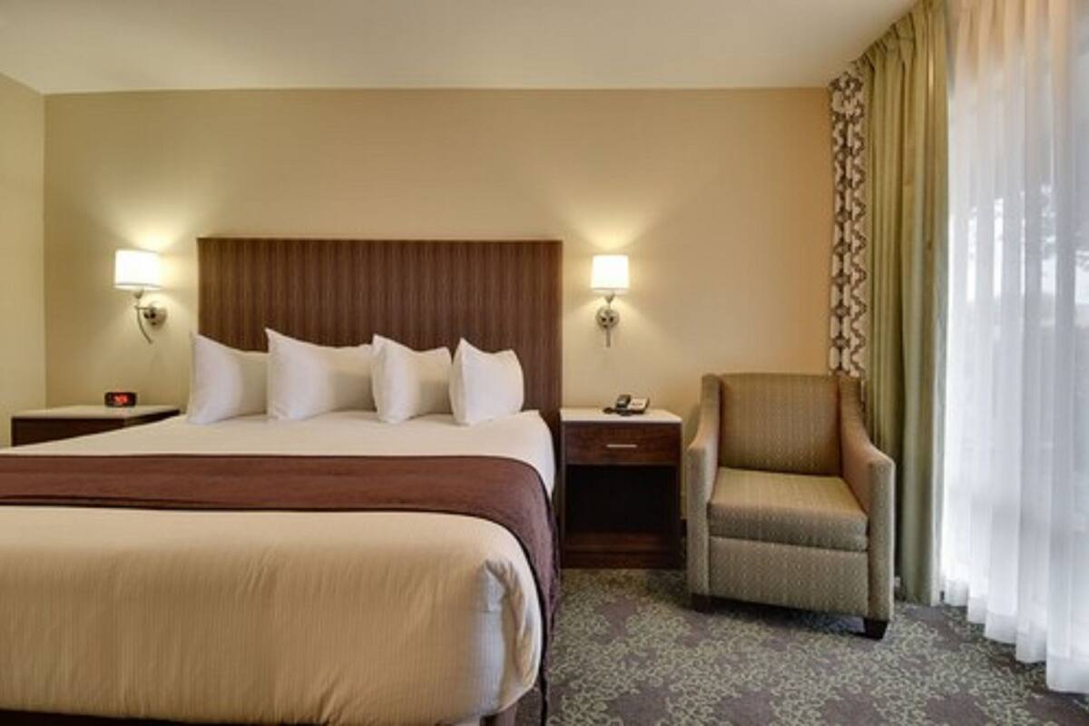 A hotel room with a large bed, two bedside tables, a chair, and a window with sheer curtains.