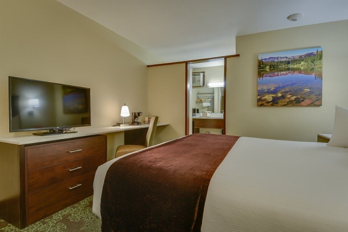 Une chambre d’hôtel avec un lit, un bureau avec une télévision, une chaise, une lampe de bureau et un tableau au mur.