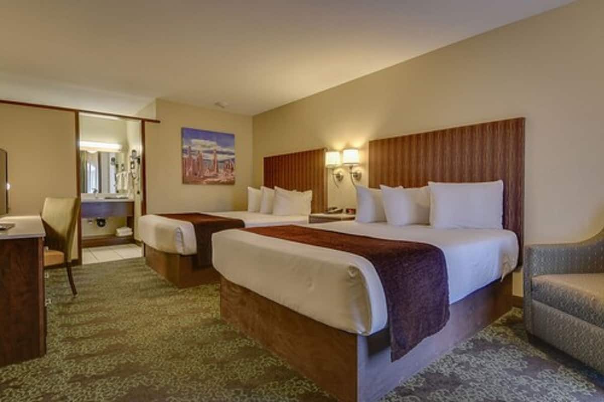 A hotel room with two beds, a desk, a chair, and a bathroom visible through an open door.