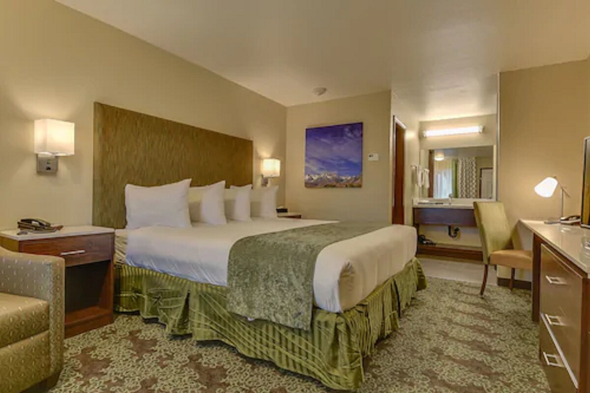 A hotel room with a large bed, bedside lamps, a desk, a chair, and a painting on the wall.
