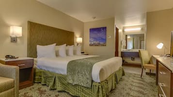 A hotel room with a large bed, bedside lamps, a desk, a chair, and a painting on the wall.
