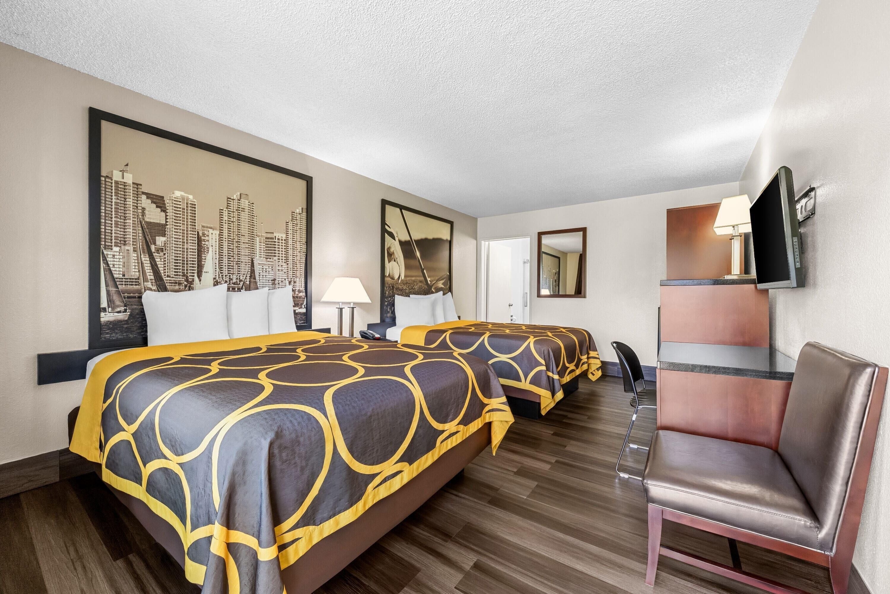 Habitación de hotel con dos camas, un escritorio, una silla y un televisor.