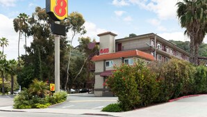 A motel with a Super 8 sign, a building with a red roof, and lush greenery around. - Super 8 by Wyndham San Diego Hotel Circle (San Diego)