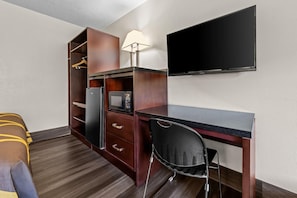A compact hotel room with a bed, a desk with a chair, a TV, a microwave, and a wardrobe.