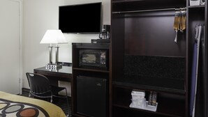 A hotel room with a bed, a desk with a lamp, a TV, a microwave, a mini-fridge, and a wardrobe with hanging items. - Super 8 by Wyndham San Diego Hotel Circle (San Diego)