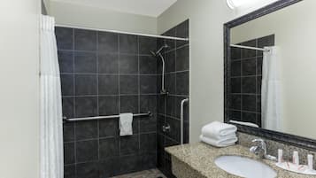 Uma casa de banho moderna com chuveiro, barra de apoio e lavatório com artigos de higiene pessoal.