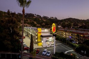 A hotel with a prominent 'Super 8' sign, a parking lot, and a hilly backdrop. - Super 8 by Wyndham San Diego Hotel Circle (San Diego)