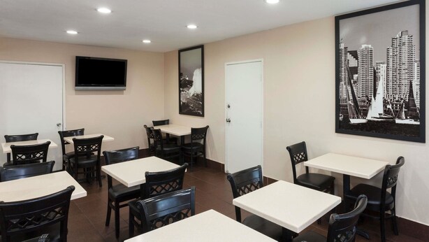 A dining area with multiple tables and chairs, a flat-screen TV mounted on the wall, and a framed cityscape picture on the wall. - Super 8 by Wyndham San Diego Hotel Circle (San Diego)