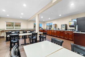 A spacious indoor dining area with multiple tables and chairs, a kitchen area with appliances, and a large screen displaying content. - Super 8 by Wyndham San Diego Hotel Circle (San Diego)