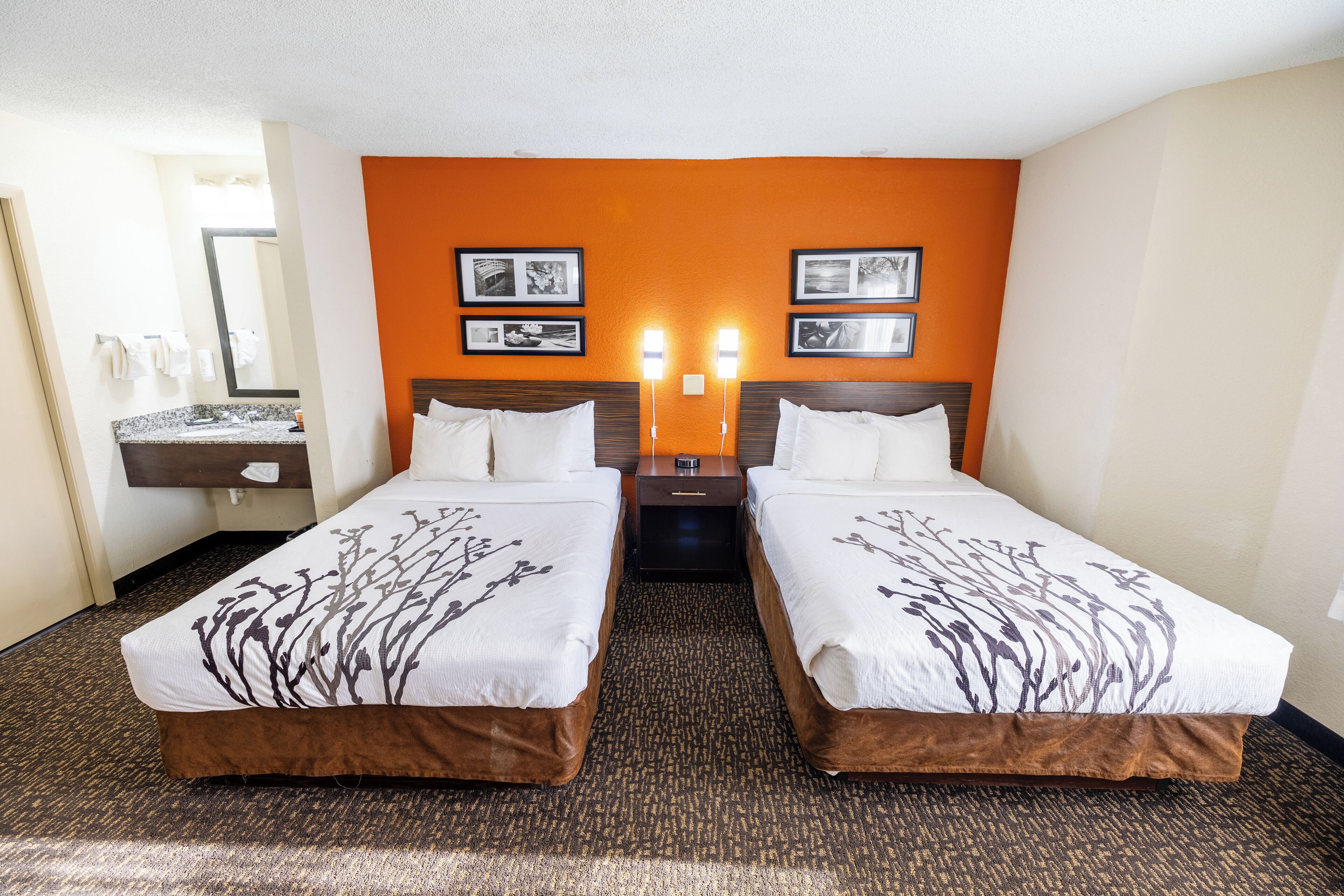 A hotel room with two beds, a bathroom, and a nightstand with a lamp.