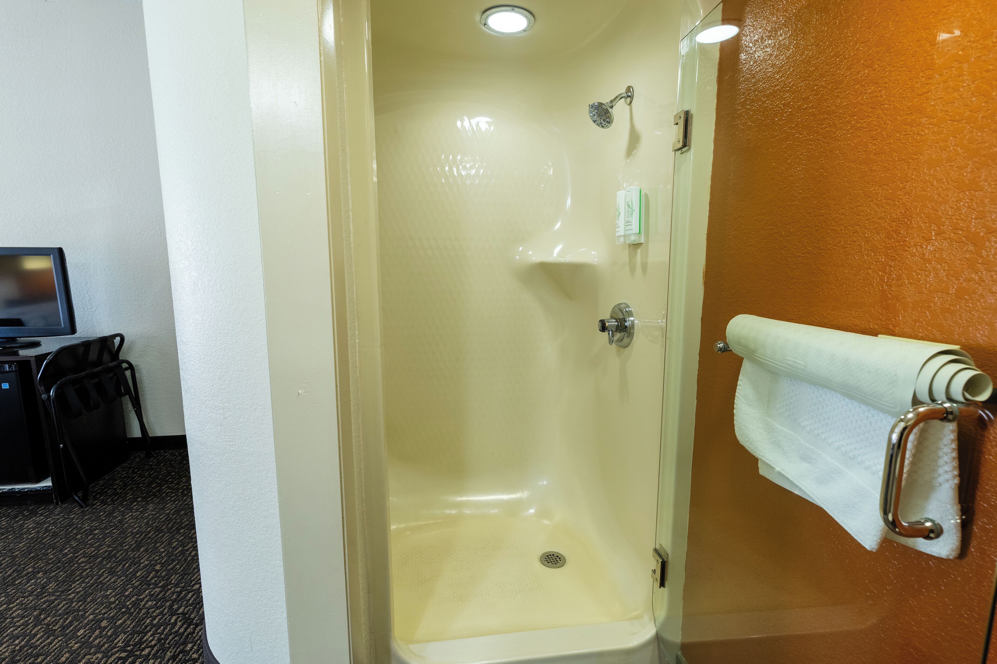 A shower with a glass door, a towel rack with a towel, and a small shelf with toiletries.