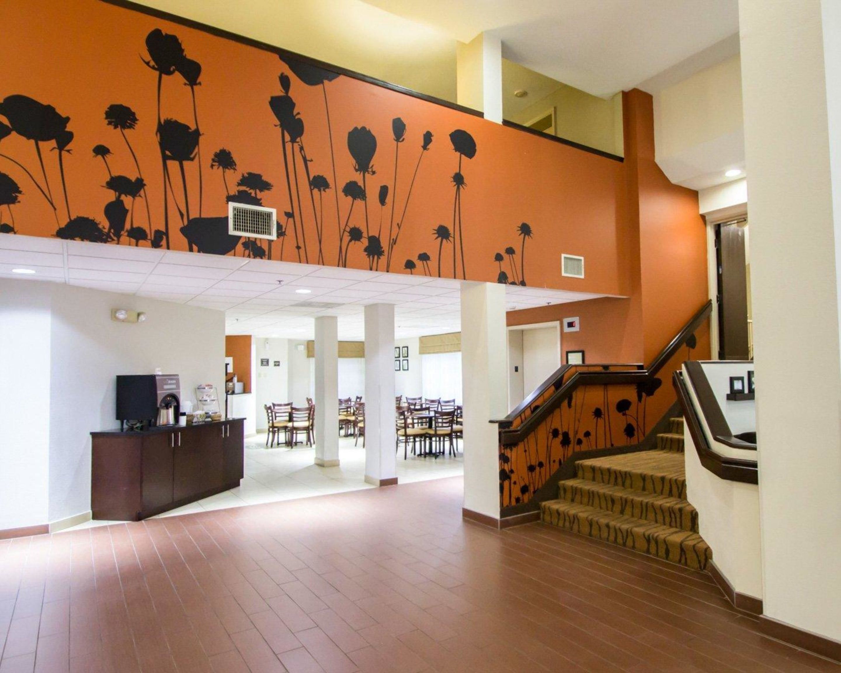 A spacious lobby with a high ceiling, a staircase with a floral design, and a reception area with chairs and a counter.