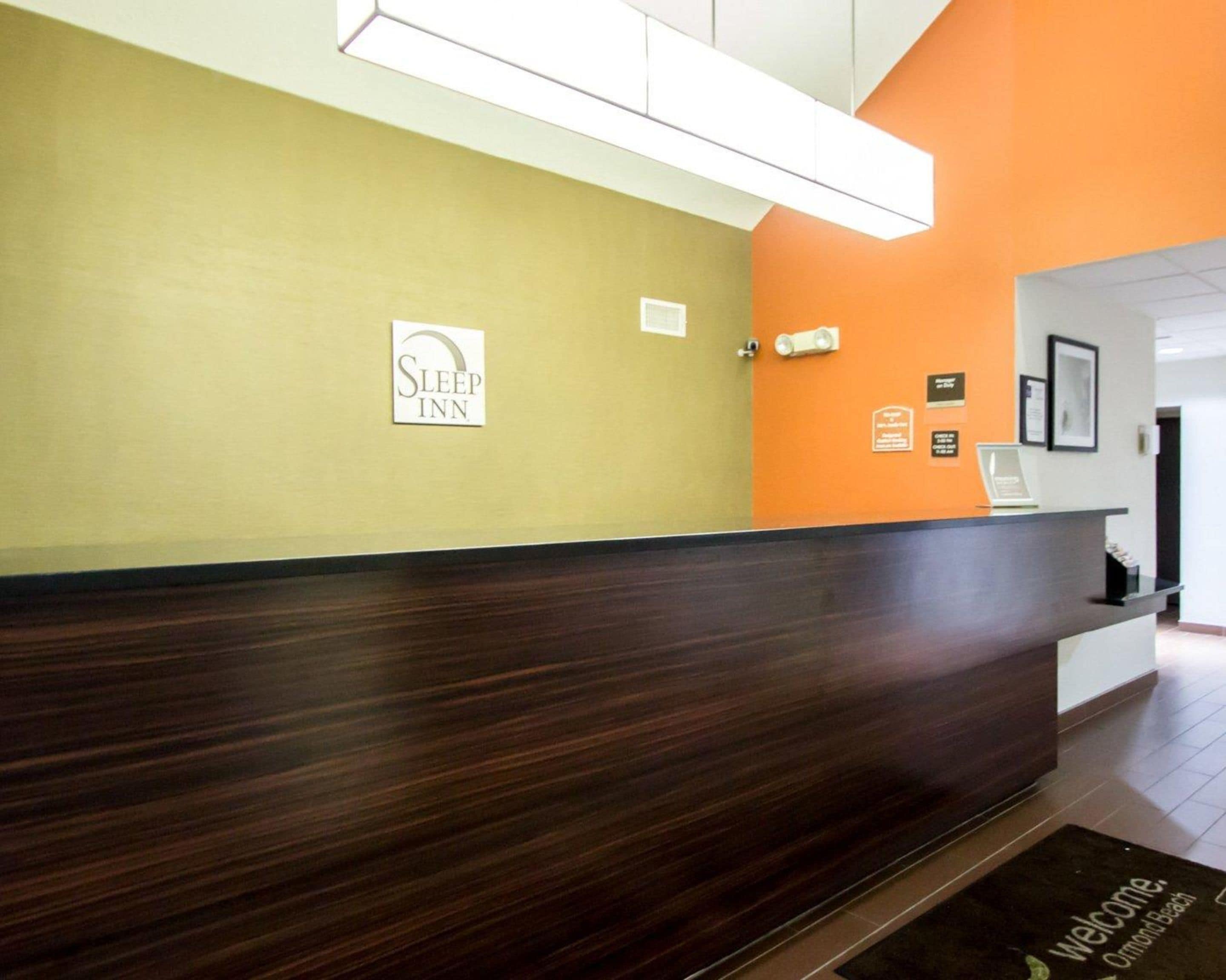A reception desk with a sign for Sleep Inn, a reception area with a dark wooden counter, and a wall with several plaques and a framed picture.
