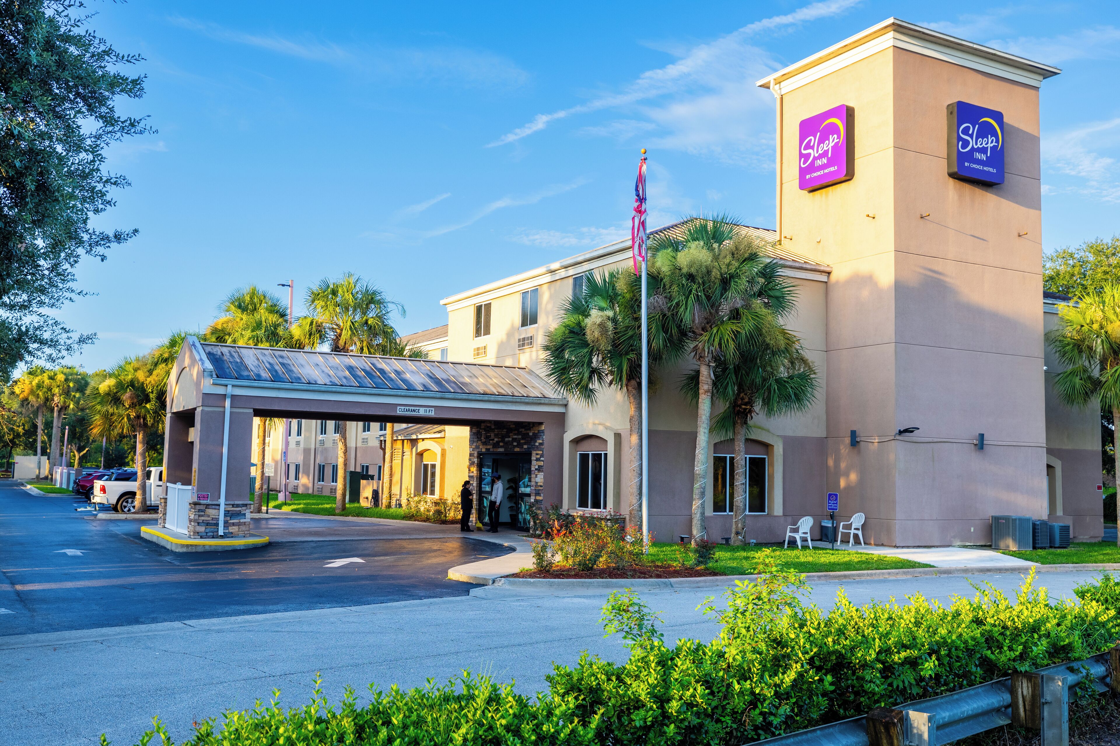 A Sleep Inn hotel with a covered entrance, palm trees, and a clear sky.