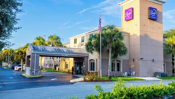 A Sleep Inn hotel with a covered entrance, palm trees, and a clear sky.