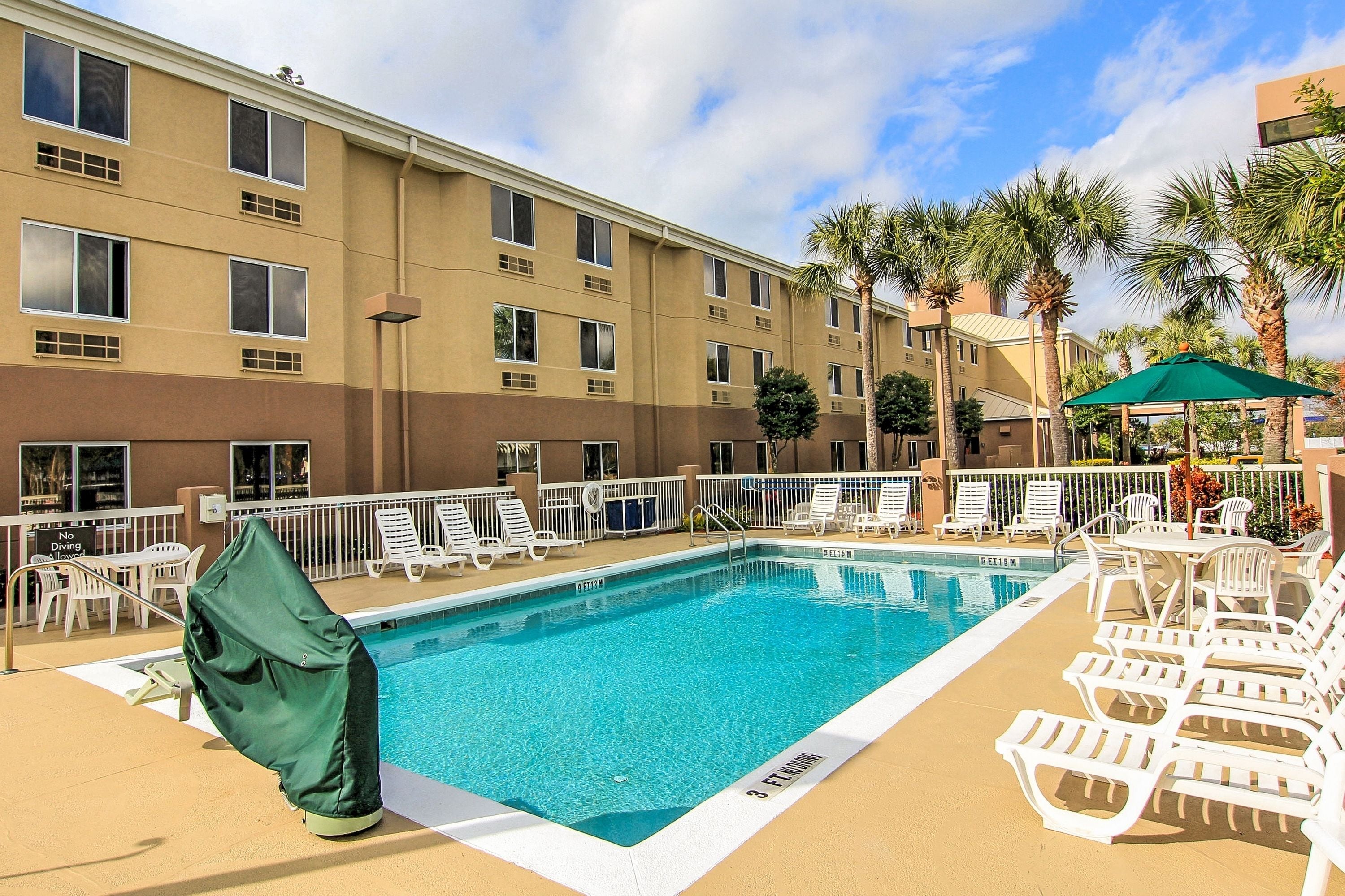A hotel pool area with a clear blue pool, white lounge chairs, and palm trees.