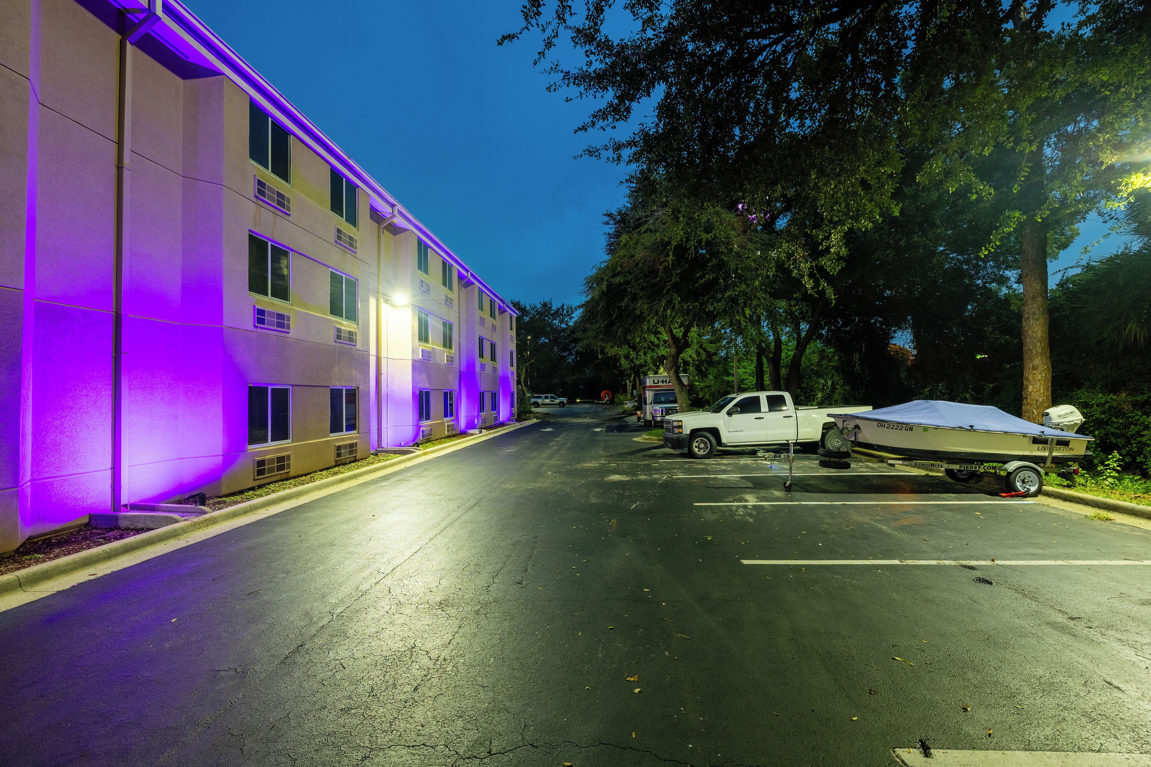 A building with purple lighting along the exterior walls, a white truck parked in front, and a boat trailer attached to the truck.