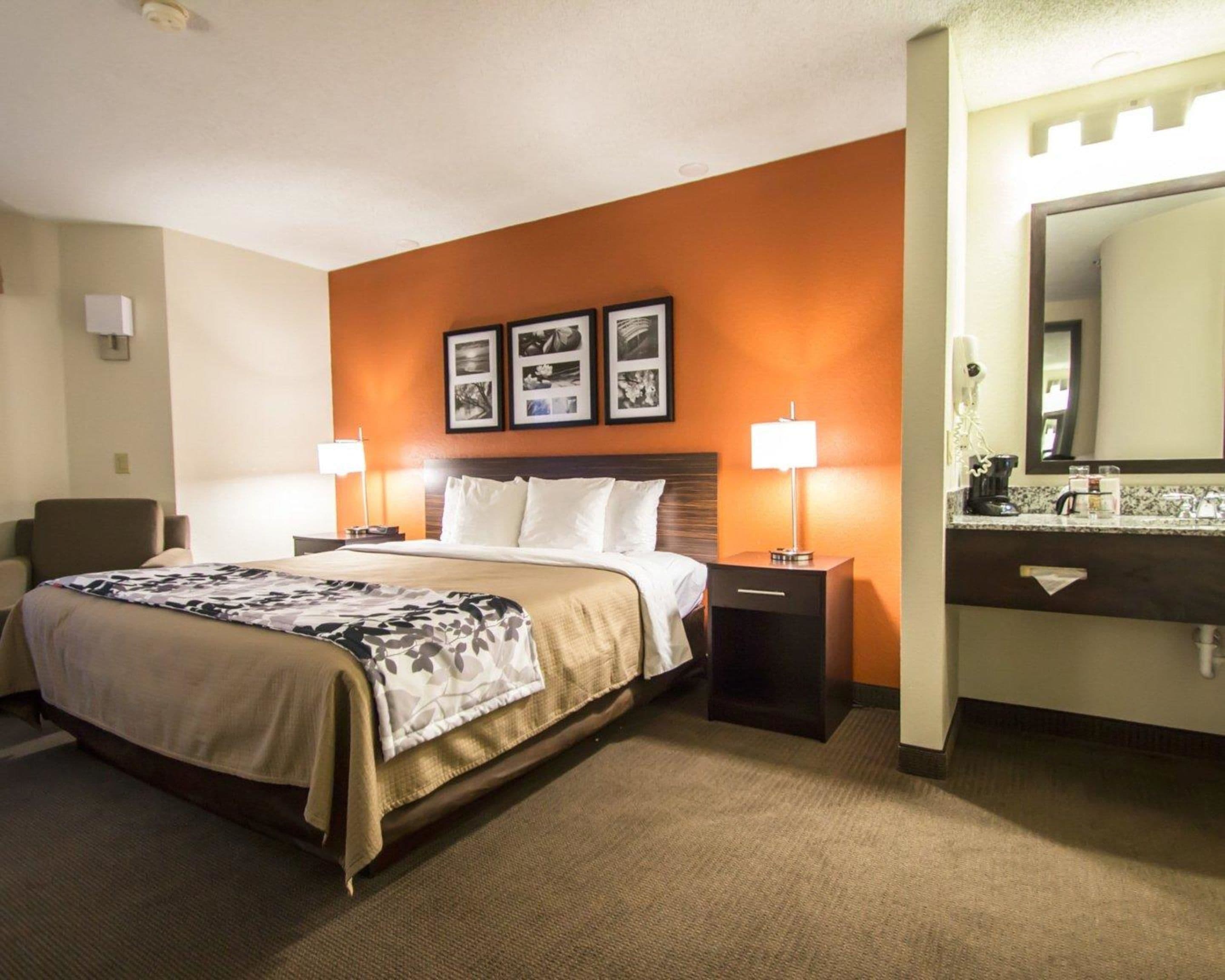 A hotel room with a bed, two bedside tables, a nightstand, a mirror, and a wall with framed pictures.
