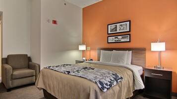 A hotel room with a bed, a chair, a nightstand with a lamp, and two framed pictures on the wall.