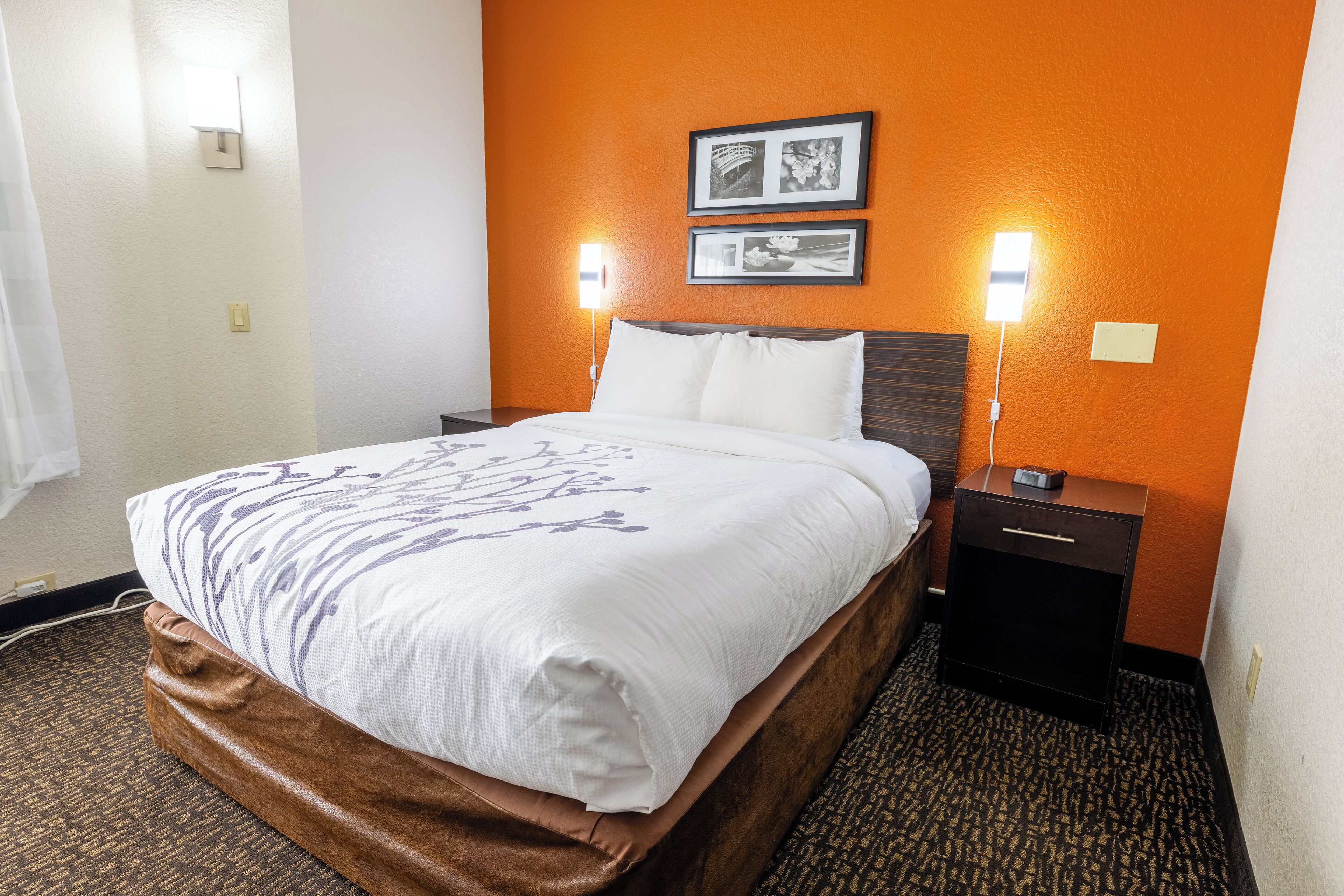 Habitación de hotel con cama, dos mesitas de noche y una lámpara de pared.