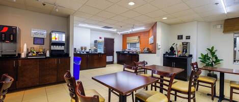A restaurant with a counter, tables, chairs, and a kitchen area.