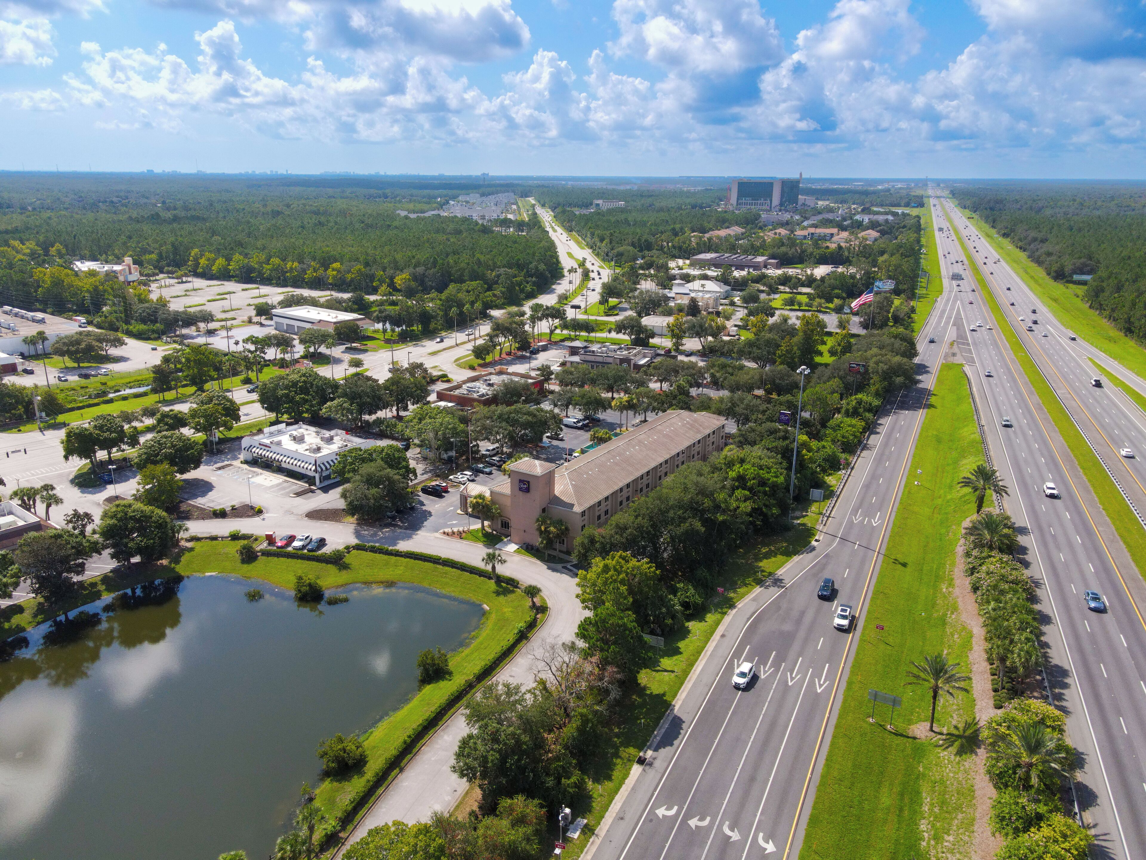 Vista aérea de una zona comercial con una autopista, estacionamientos y un edificio grande con techo plano.