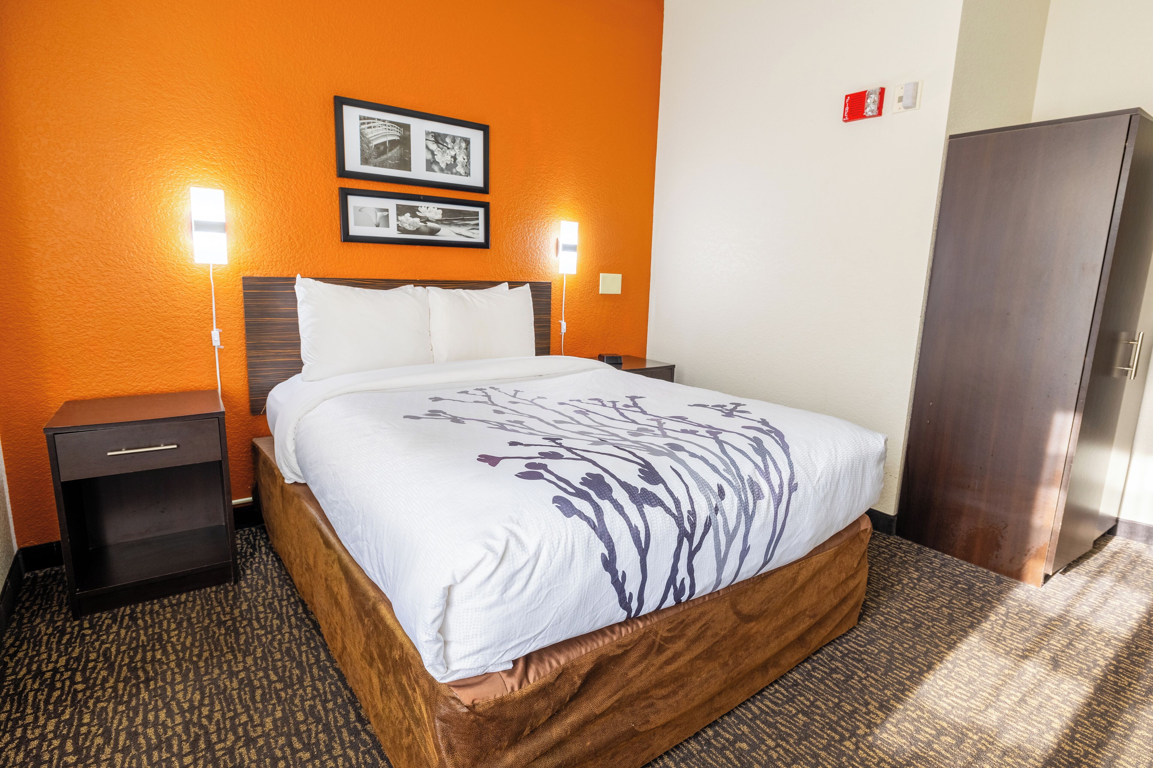 A hotel room with a bed, two bedside lamps, a nightstand, a wardrobe, and two framed pictures on the wall.