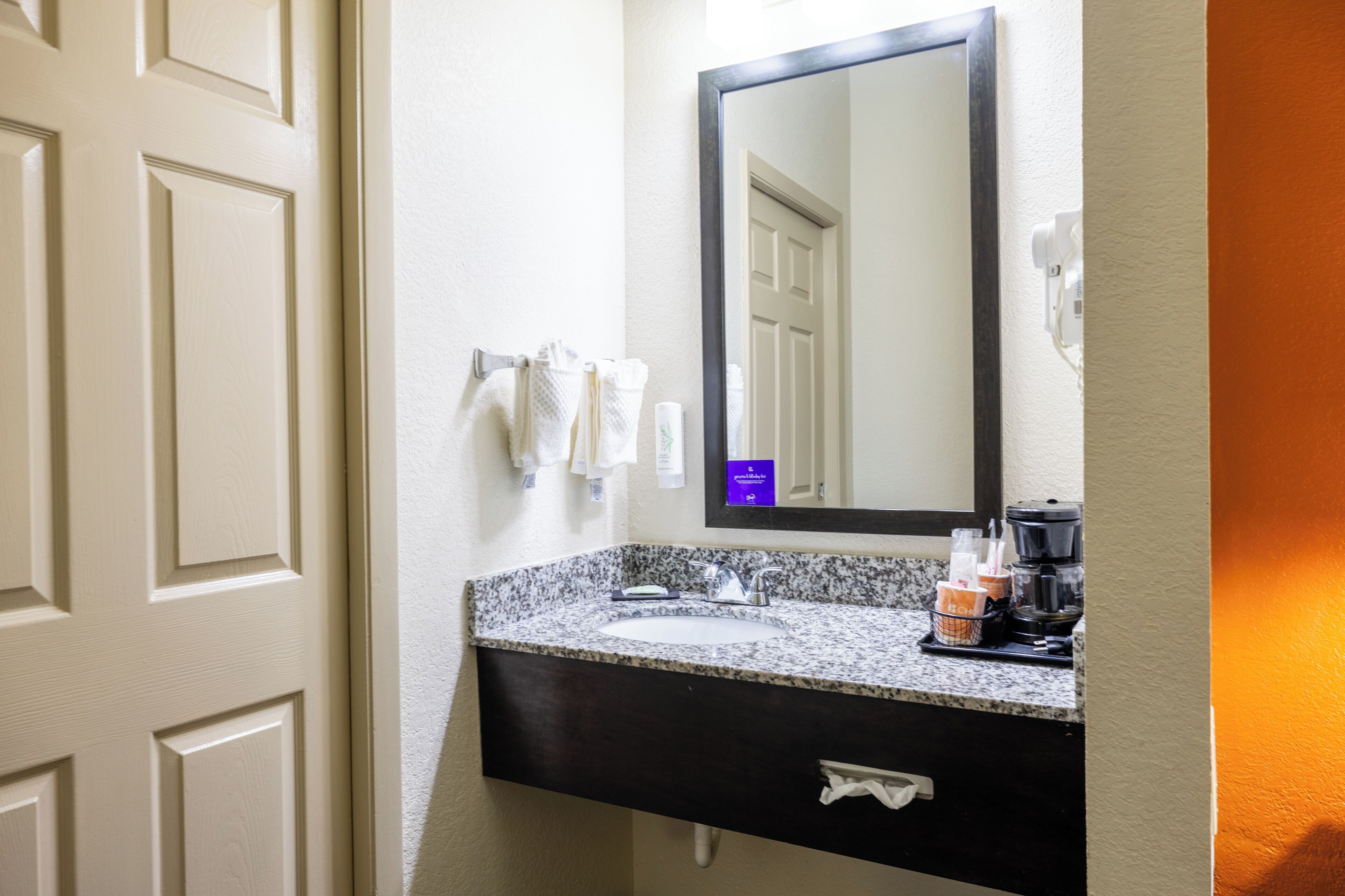A bathroom with a white door, a granite countertop sink, a dark cabinet, and a mirror above the sink.
