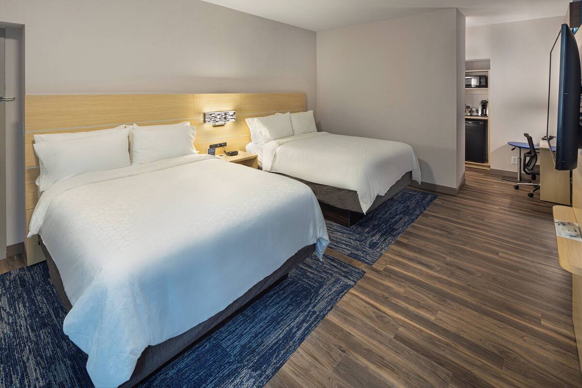 A hotel room with two beds, a wooden headboard, a desk with a chair, and a television.