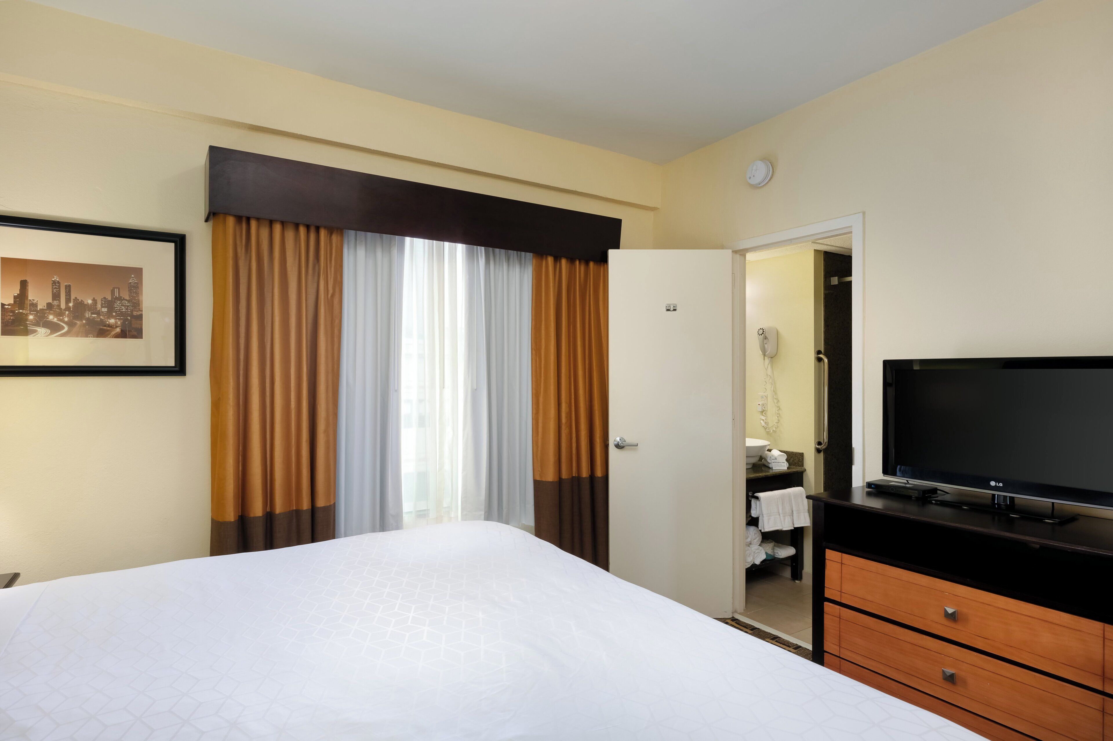 A hotel room with a bed, a television, a bathroom with a mirror, and a door leading to another room.