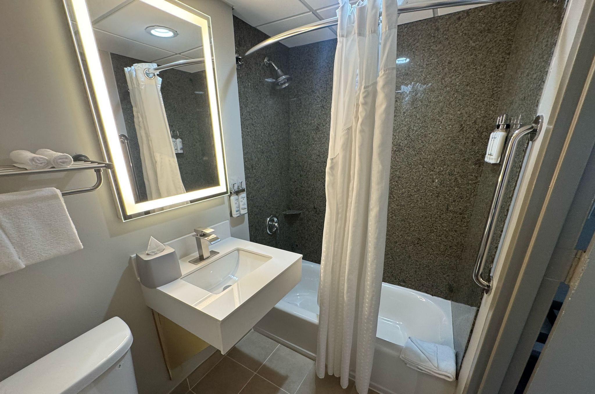 Une salle de bain moderne avec un lavabo, un miroir et des toilettes blancs. On y trouve un espace douche avec une porte en verre et une baignoire.