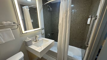 Une salle de bain moderne avec un lavabo, un miroir et des toilettes blancs. On y trouve un espace douche avec une porte en verre et une baignoire.