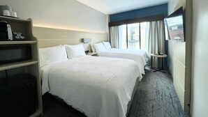 Une chambre d’hôtel avec deux lits, une table de chevet avec une lampe, une télévision et une étagère avec une machine à café et d’autres objets.