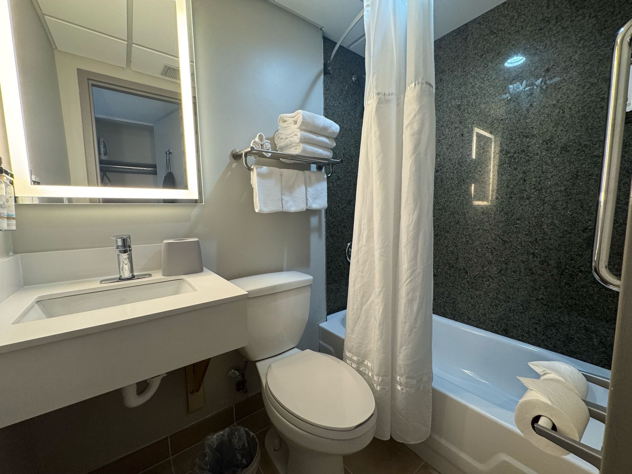 A modern bathroom with a white sink, toilet, and bathtub. There is a towel rack with folded towels and a shower curtain.