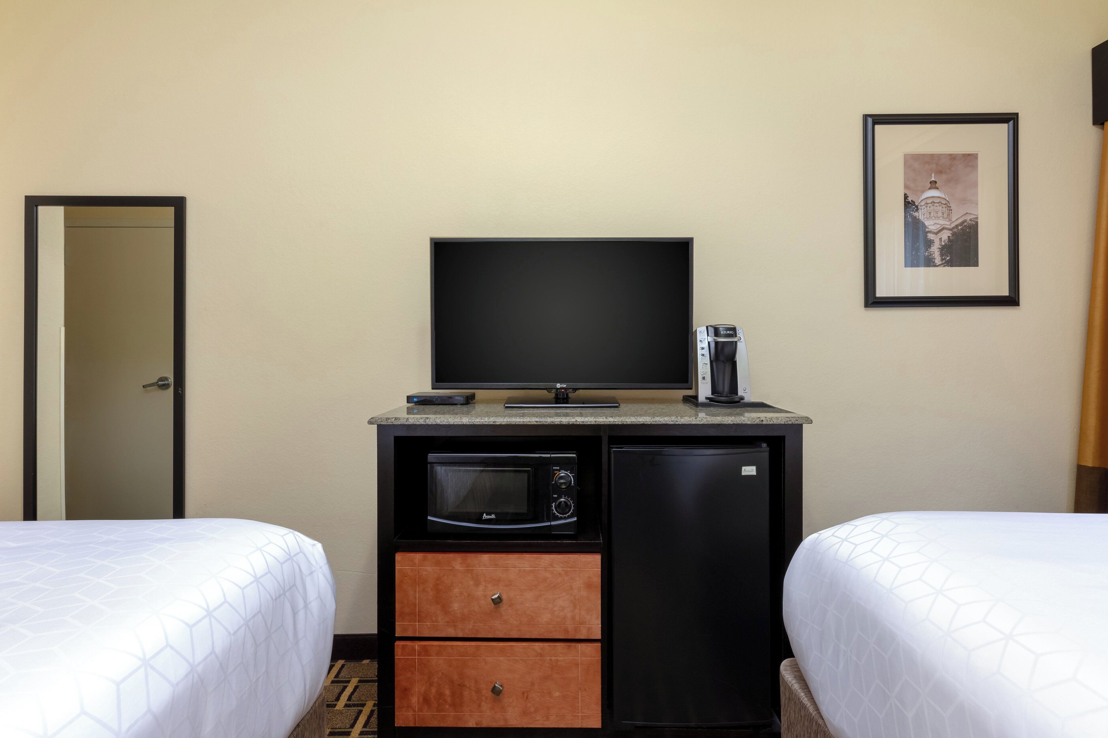 A hotel room with two beds, a television, a coffee maker, a microwave, and a small refrigerator.