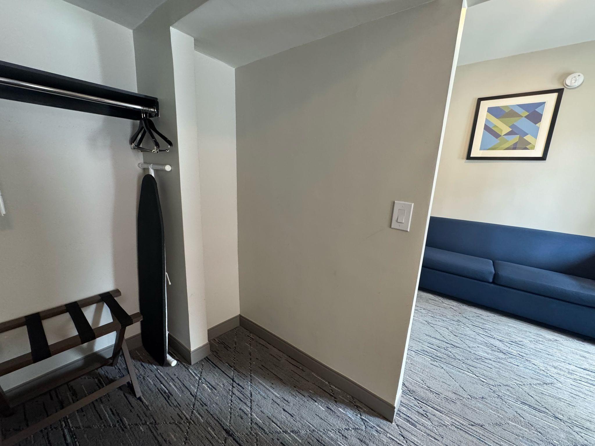 A room with a wooden bench, a coat rack, a blue sofa, and a framed abstract painting on the wall.
