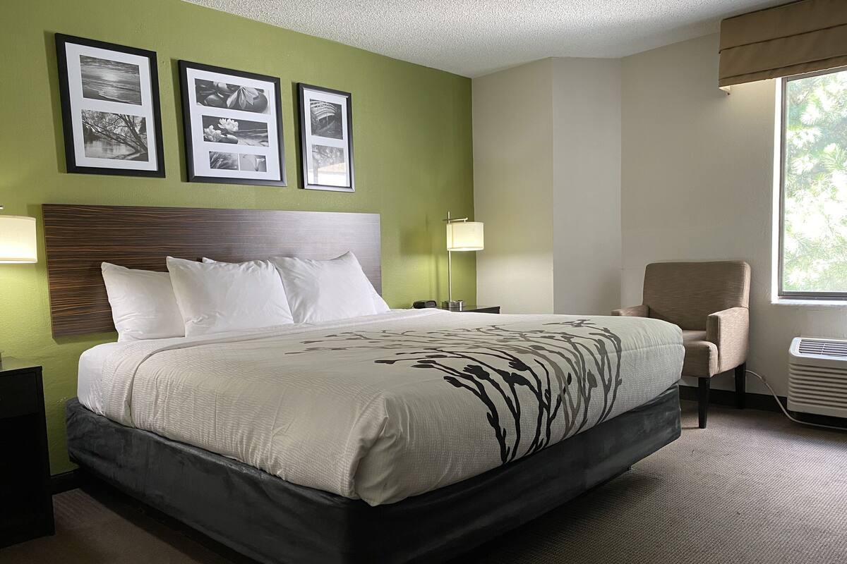A hotel room with a large bed, a chair, and three framed pictures on the wall.