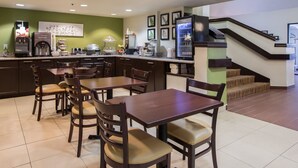Zona de dinar d'un hotel amb barra de cuina, màquines de cafè i un frigorífic.