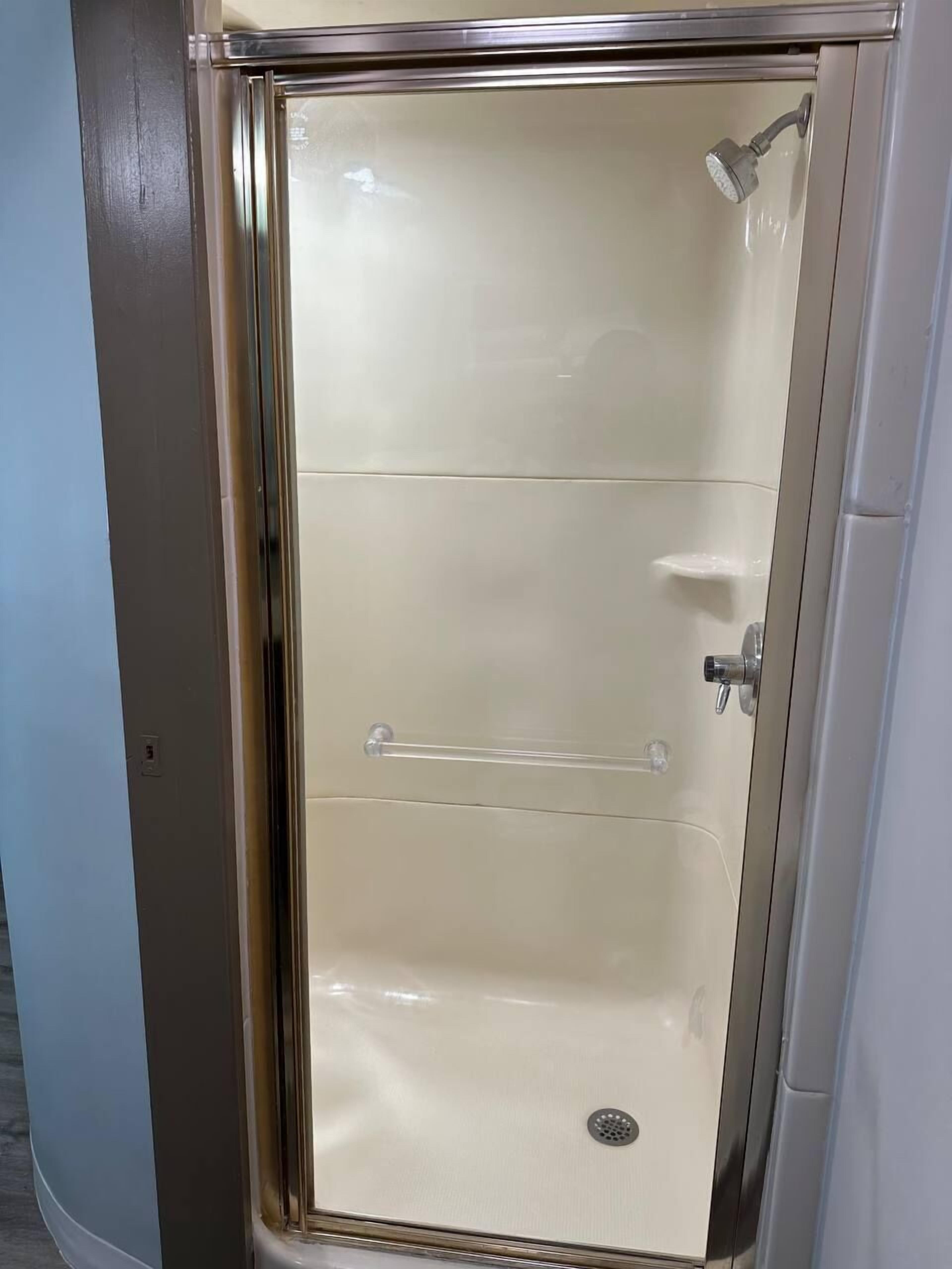 A small, enclosed shower area with a glass door, a showerhead, and a handrail.