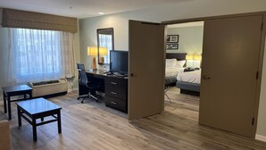 Une chambre d’hôtel avec un bureau, une chaise et un lit. Il y a une fenêtre avec des rideaux, une lampe et un miroir sur le mur.