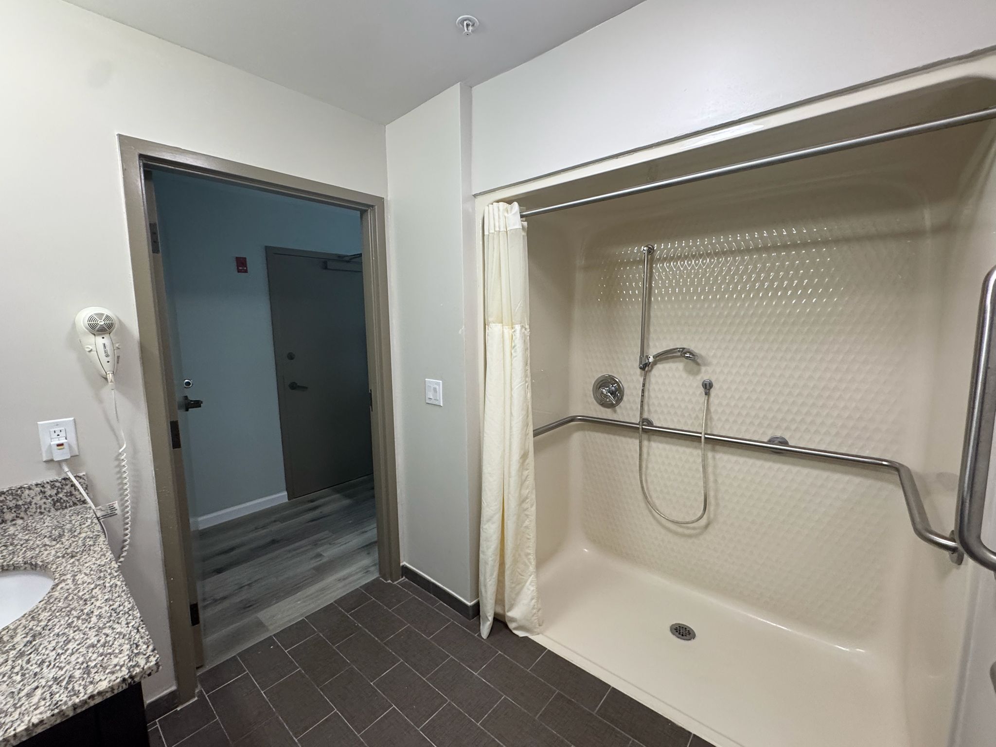 Un baño con ducha, lavamanos y puerta que da a otra habitación.