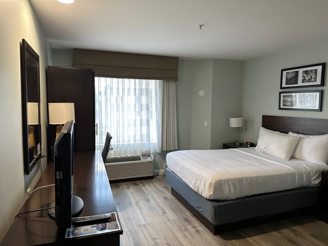Habitación de hotel con cama, escritorio con computadora, televisión y ventana con cortinas.