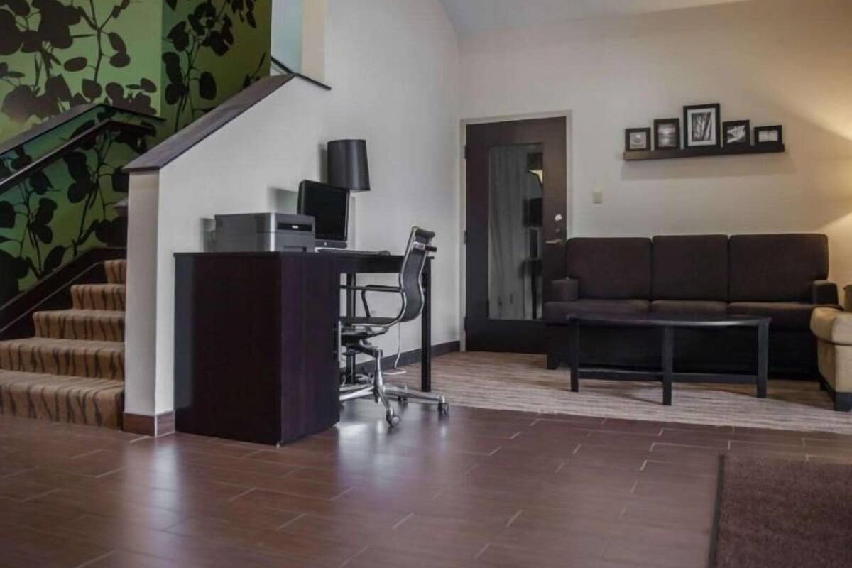 Ein modernes Wohnzimmer mit Treppe, Schreibtisch mit Computer, Sofa und Couchtisch.